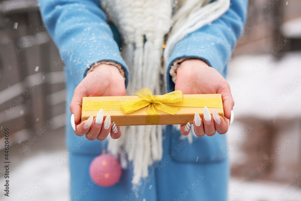 Woman holding a small gift box at the street with a snowfall