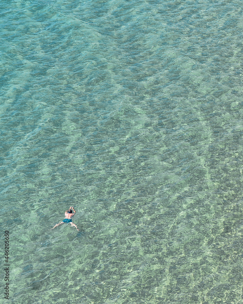 Hombre nadando en aguas cristalinas con bañador azul en el mar mediterráneo