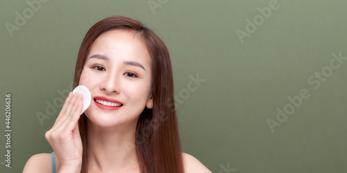 Beautiful young woman with silky skin using cotton pads on green background