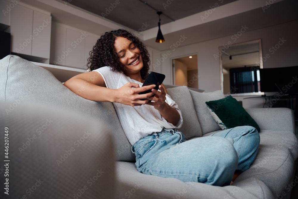 Happy mixed race female teenager relaxing at home typing on cellular device  sitting on couch Stock-Foto | Adobe Stock