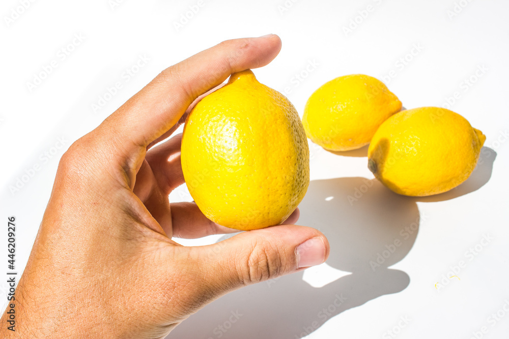 A fresh bright lemon fruit held by hand against a group of lemons in the background A fresh bright lemon fruit held by hand against a group of lemons in the background