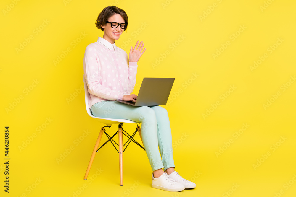 Full length body size photo of girl waving hand during video connection on computer isolated vivid yellow color background Full length body size photo of girl waving hand during video connection on computer isolated vivid yellow color background