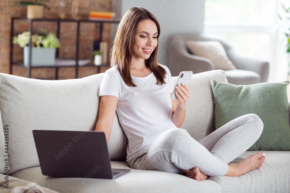 Photo portrait brunette woman sitting on couch at home browsing internet with smartphone near laptop Photo portrait brunette woman sitting on couch at home browsing internet with smartphone near laptop