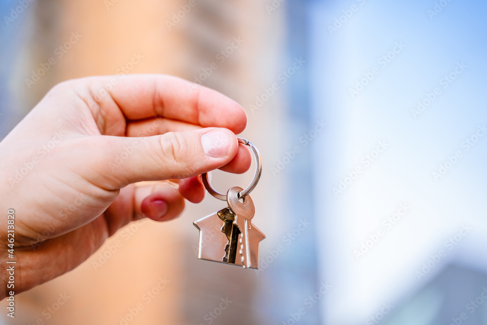 A man's hand holds the keys to a new house against the background of high-rise buildings
