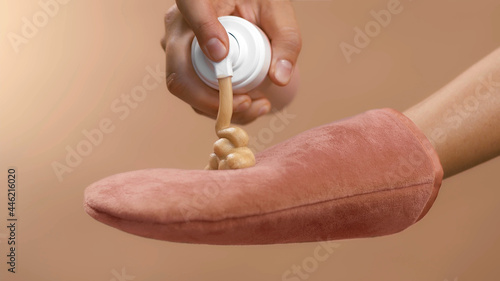 Dosing bronzing lotion or tanning cream from a flask with a doser to a pink tan applicator glove. High quality close-up studio photo image beige background. photo