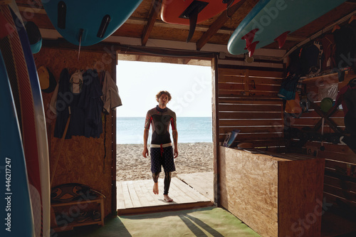 Surfer entering to wooden hut on sandy beach