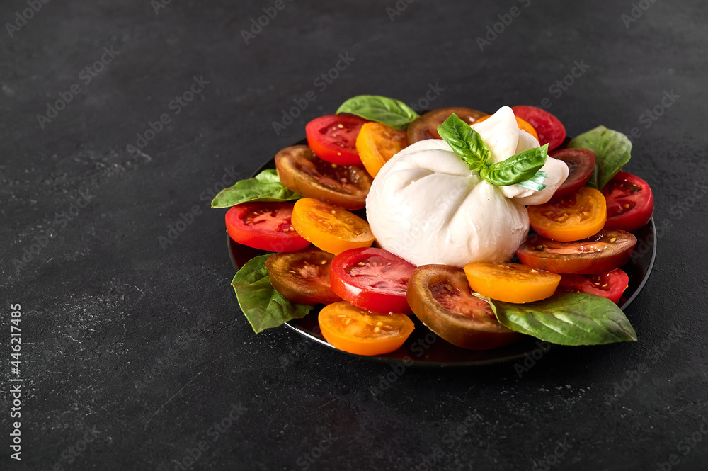 Salad with italian burrata cheese with basil and tomato on dark textured background. Close up