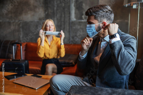 Business people put on face masks during a corona pandemic while sitting in the hotel lobby before the meeting begins. They are on a business trip. Covid, protection