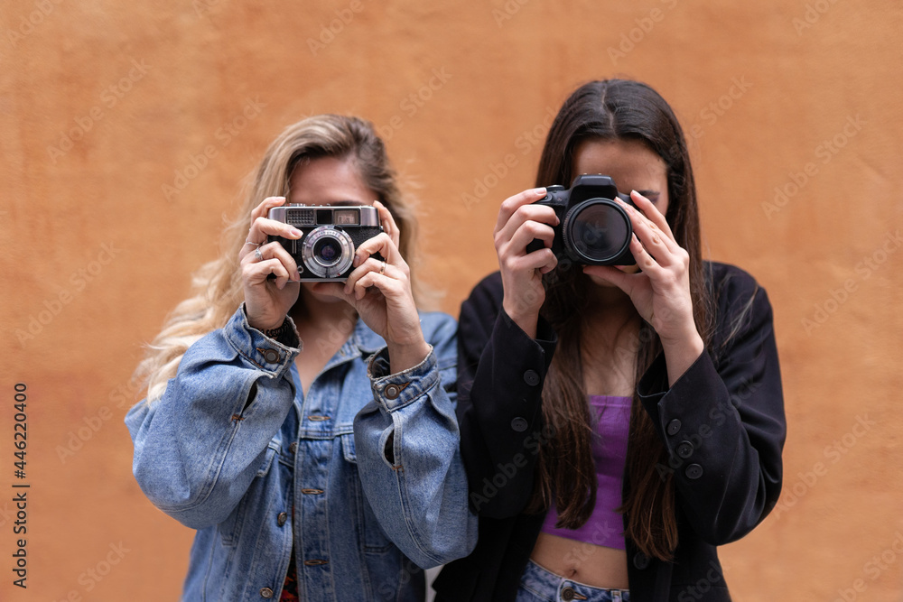Two photographer girls using analog and digital cameras with an orange background