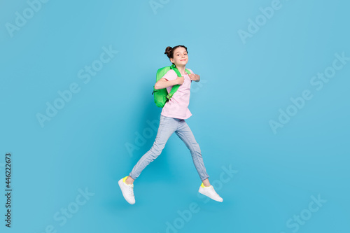 Photo of shiny pretty school girl wear pink t-shirt backpack smiling walking jumping high isolated blue color background