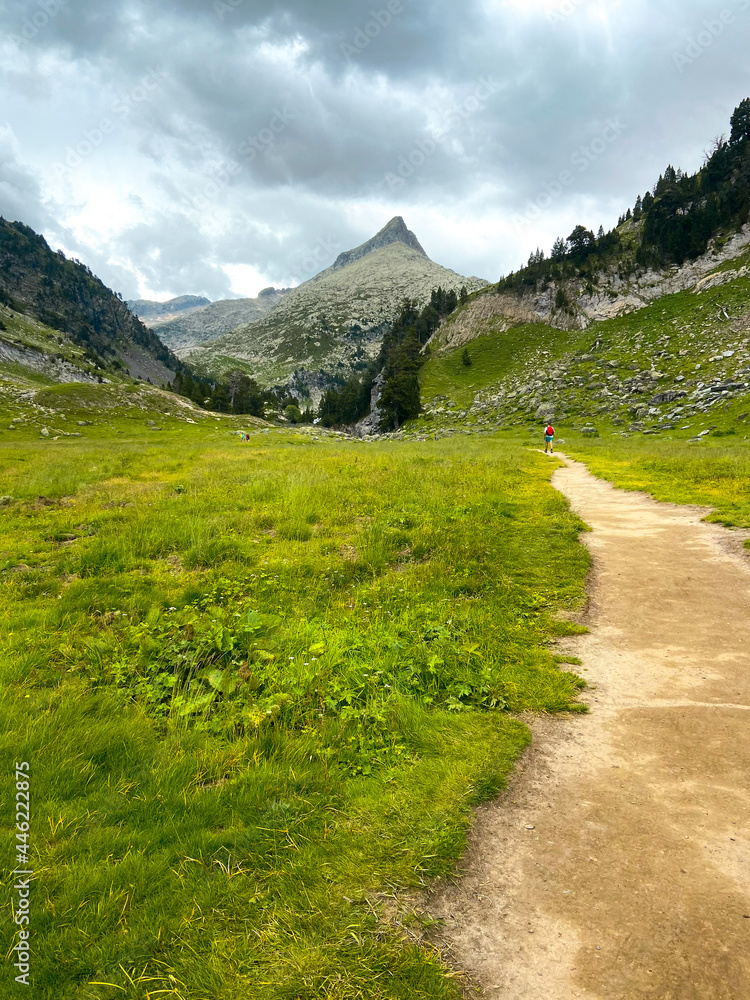 Young boy hiking and walking alone in the distance through a mountainous natural landscape in Pyrenees.