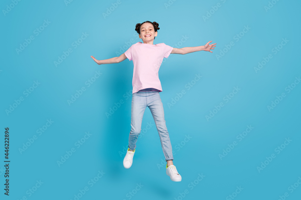 Photo of charming pretty school girl wear pink t-shirt smiling jumping high arms sides isolated blue color background Photo of charming pretty school girl wear pink t-shirt smiling jumping high arms sides isolated blue color background