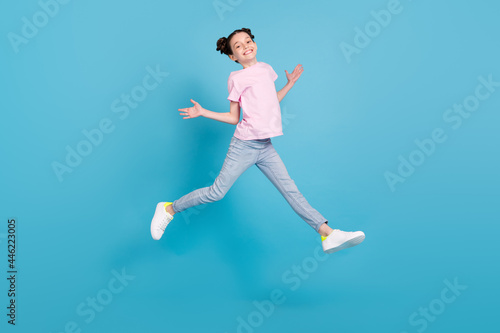 Photo of pretty funky school girl wear pink t-shirt smiling jumping high arms sides isolated blue color background