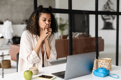 Photos Black young woman doing facial massage while using laptop at home