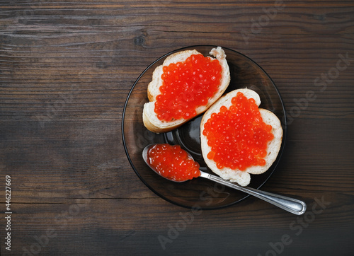 Delicious fresh red caviar, sandwiches, plate and spoon on wood table background. Top view. Flat lay.
