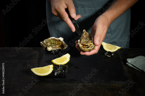 Photos A man's hands are shucking fresh oysters with a blade of knife, Opening the hollow and flat oysters