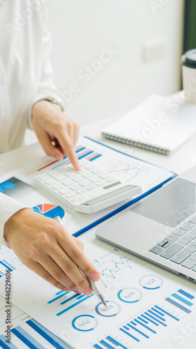 A young financial market analyst works in the office on his laptop while sitting at a wooden table. Businessman analyzing documents in hand Graph and financial concept calculator with vertical images.