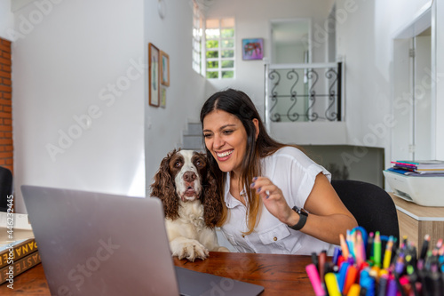 Smiling latina woman having video call via laptop in home office showing her dog
