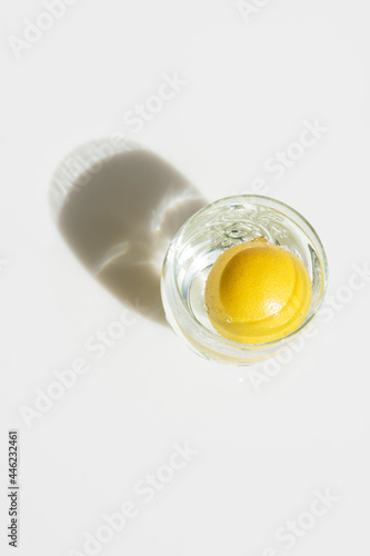 Whole yellow lemon in a glass of water in bright sunlight with drop shadow. Hydration detox healthy lifestyle concept