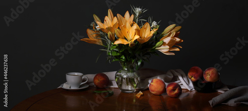 Panorama still life with a bouquet of flowers, peaches and a cup of coffee on a dark background