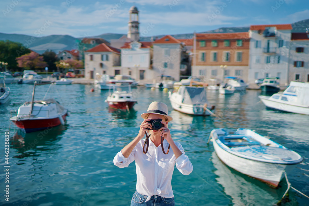 Photography and travel. Young woman taking photo with her camera on the sea beach near fishing boats in old town on Dalmatia coast, Croatia.