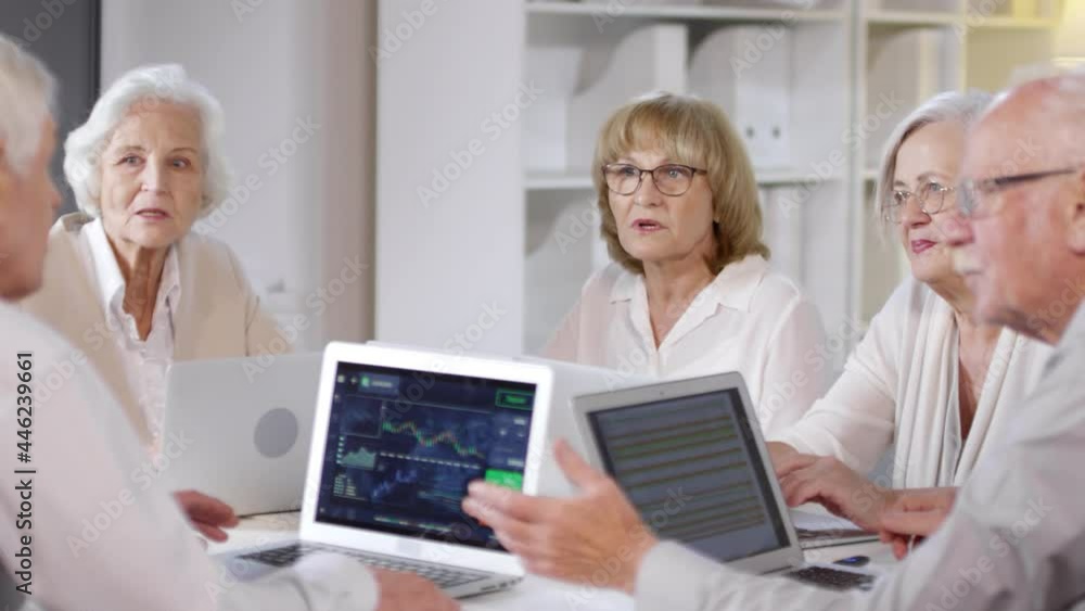 PAN shot of group of senior people with laptops discussing work in office PAN shot of group of senior people with laptops discussing work in office