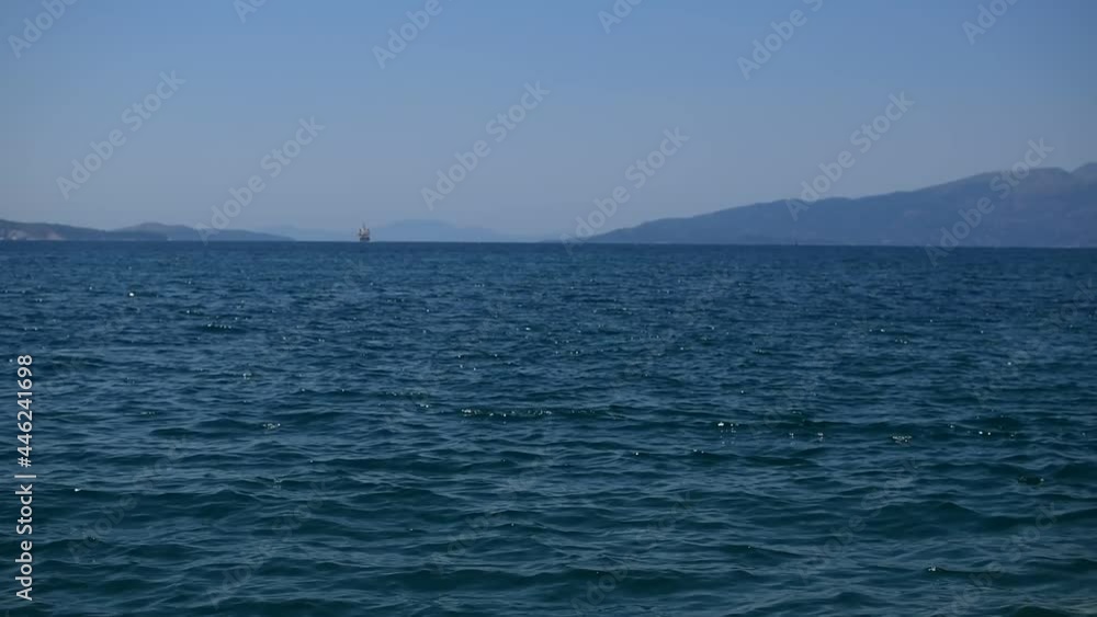 Blue sea with reflections of waves against blurred background of mountains and silhouette of a ship on horizon Blue sea with reflections of waves against blurred background of mountains and silhouette of a ship on horizon