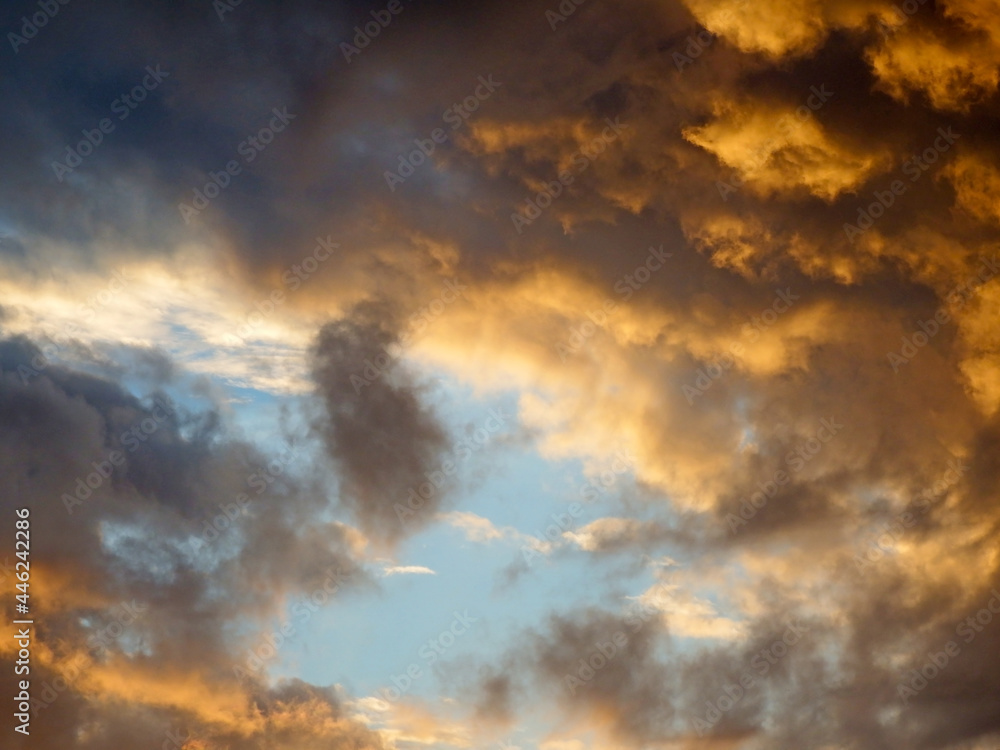 Fototapeta premium Skyscape background of a changing sky with dark and orange sunlit clouds gathering