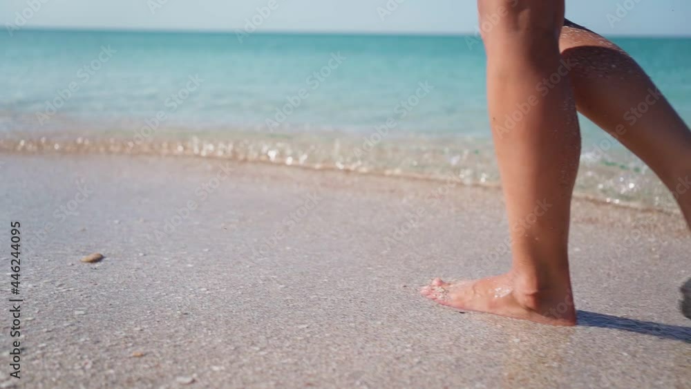 Slim Girl Legs Walking along the Sandy Beach along the Transparent Turquoise Sea. Unrecognizable Pretty Woman Walks at Seaside Surf. Summer Vacation and Travel. Slow motion. Slim Girl Legs Walking along the Sandy Beach along the Transparent Turquoise Sea. Unrecognizable Pretty Woman Walks at Seaside Surf. Summer Vacation and Travel. Slow motion.