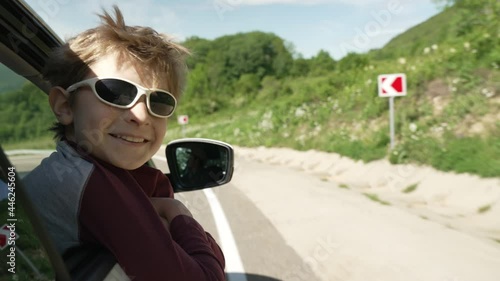 Boy putting his head and hands out of the car window driving down a mountain road. Dreaming boy look out from the car window to nature. Travel with parents.
