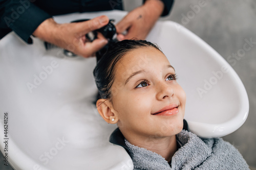 Young girl enjoying at hairstyle treatment while professional hairdresser gently washing her hair.