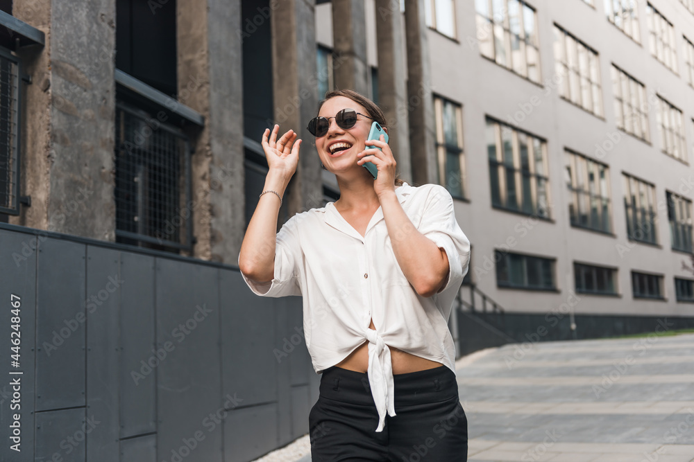 Close up emotion girl walking with smartphone in urban background. Smiling lady holding cellphone in hands outside. 