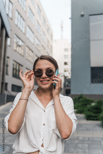 Close up emotion girl walking with smartphone in urban background. Smiling lady holding cellphone in hands outside.  © Petryshak