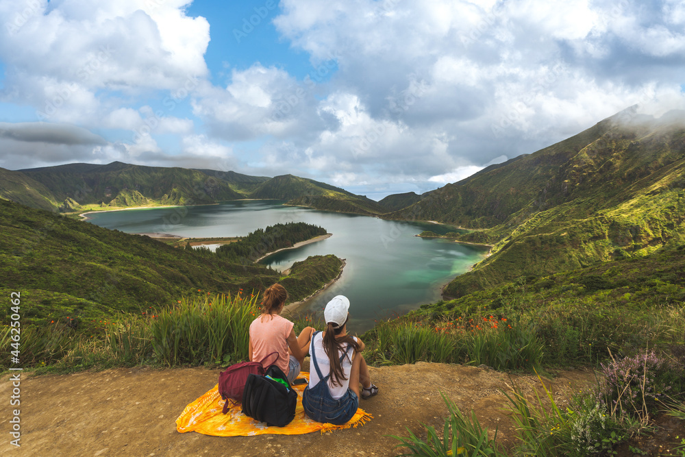 Rear view of two friends on hill top against beautiful summer landscape with forest and lake in summer. Tourists admiring wonderful nature in Azores. Vacation concept