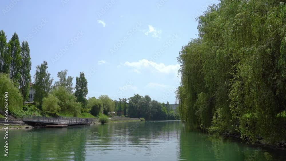 Navigating on Ljubljanica river in Ljubljana city, Slovenia. Unique perspective of green suburb on hot summer day. Trees covering river bank. Real time, forward moving, wide angle Navigating on Ljubljanica river in Ljubljana city, Slovenia. Unique perspective of green suburb on hot summer day. Trees covering river bank. Real time, forward moving, wide angle