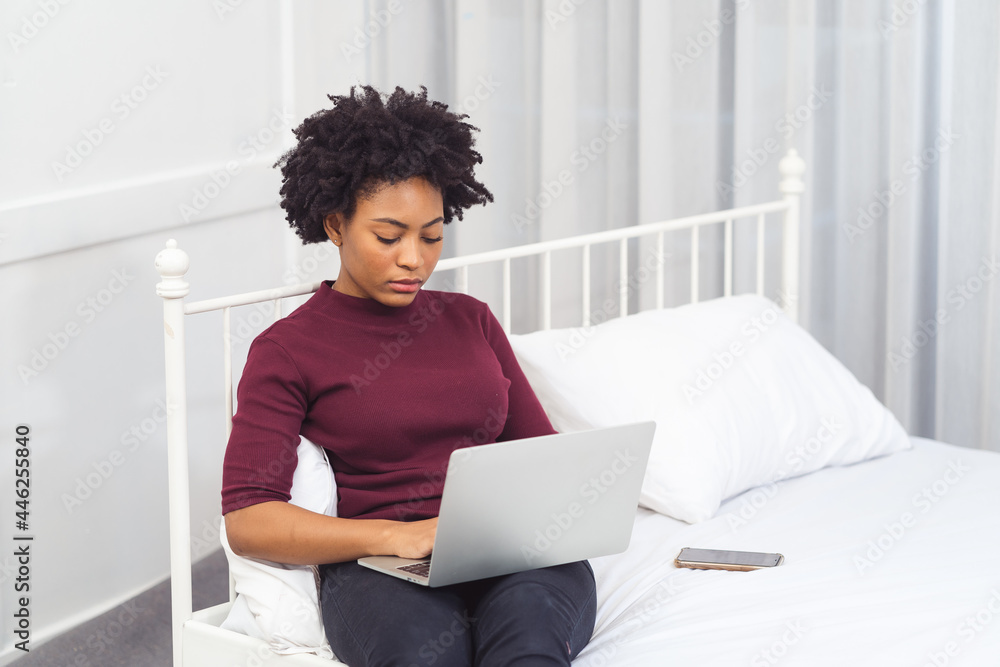 Happy casual beautiful american african woman working on laptop computer while setting on the bed in the house. Happy casual beautiful american african woman working on laptop computer while setting on the bed in the house.