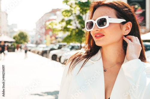 Portrait of young sexy modern businesswoman model. Hot beautiful woman in white suit posing on the street background. Fashion female walking outdoors in sunglasses