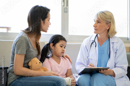 Pediatrician doctor examining little asian girl with a broken arm wearing a cast at hospital