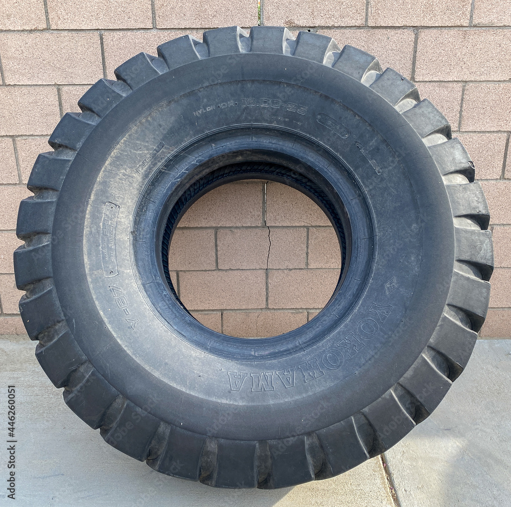huge single truck tractor rubber industrial tire wheel isolated against a block wall