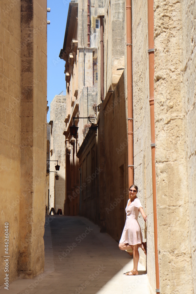 Woman in long dress walking old town of Valletta, sands and ruins tiny square streets