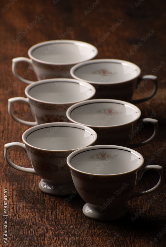 Porcelain cups, beautiful porcelain cups geometrically arranged on rustic wood, dark background, selective focus. Porcelain cups, beautiful porcelain cups geometrically arranged on rustic wood, dark background, selective focus.