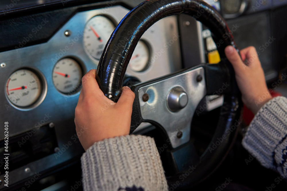 Fototapeta premium Hands of a kid on a steering wheel, while he plays a racing game in a realistic looking racing . little child driving a virtual sports car in a toy machine. horizontal