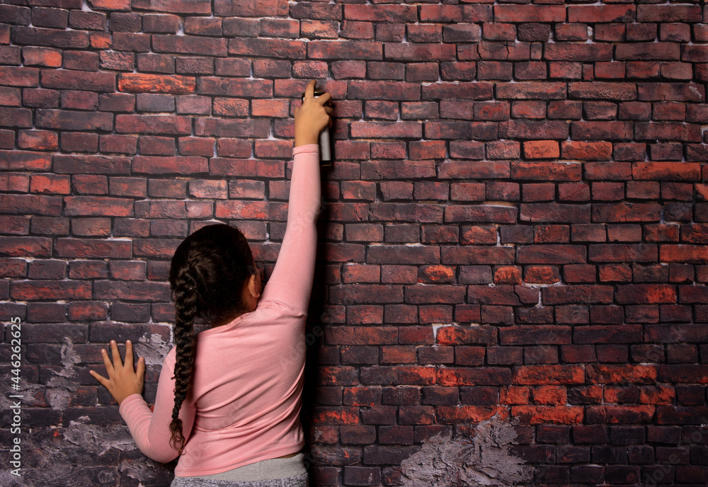 Small girl doing poses with a spray in front of an old brick wall backdrop, dark background, selective focus.
