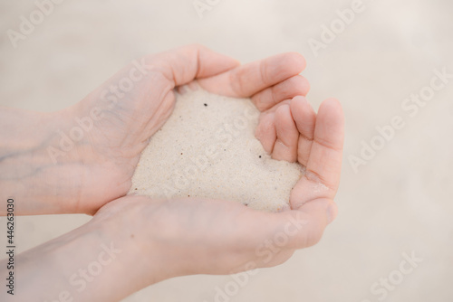 Women's hands hold white beach sand.
