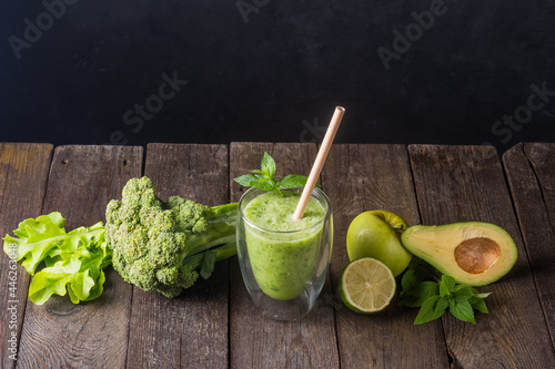 Fresh green smoothie in glass on wooden table, closeup.  Detox diet concept: green vegetables on rustic table. Clean eating, alkaline diet, weight loss food concept. photo