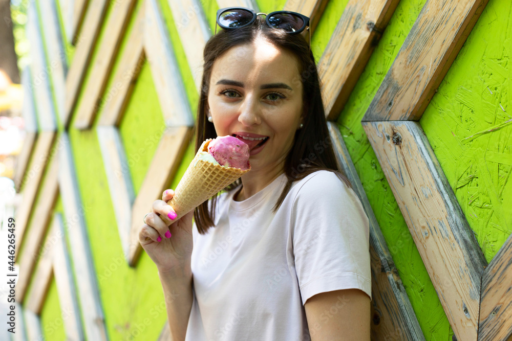 A young woman is standing near the wall eating ice cream, walking in the park. A young woman is standing near the wall eating ice cream, walking in the park.