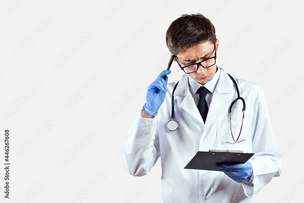 Fototapeta premium Doctor with a stethoscope on a white background. A man in a medical gown with glasses. The doctor is surprised with a tablet in his hands.