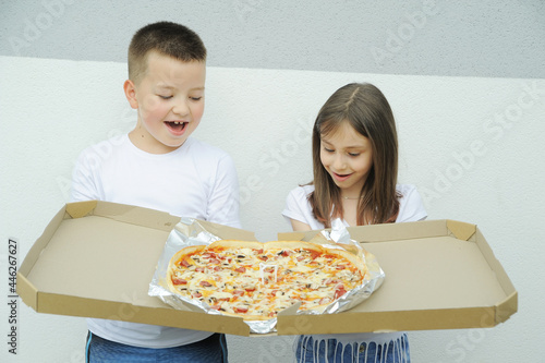 Cute girl and a boy eating a big delicious pizza outdoors 