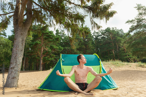 Young man sitting by tent ant posing