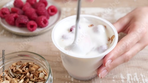 Plain yogurt with granola and raspberries in plastic jar on wooden table. Eating healthy food, snack or diet meal